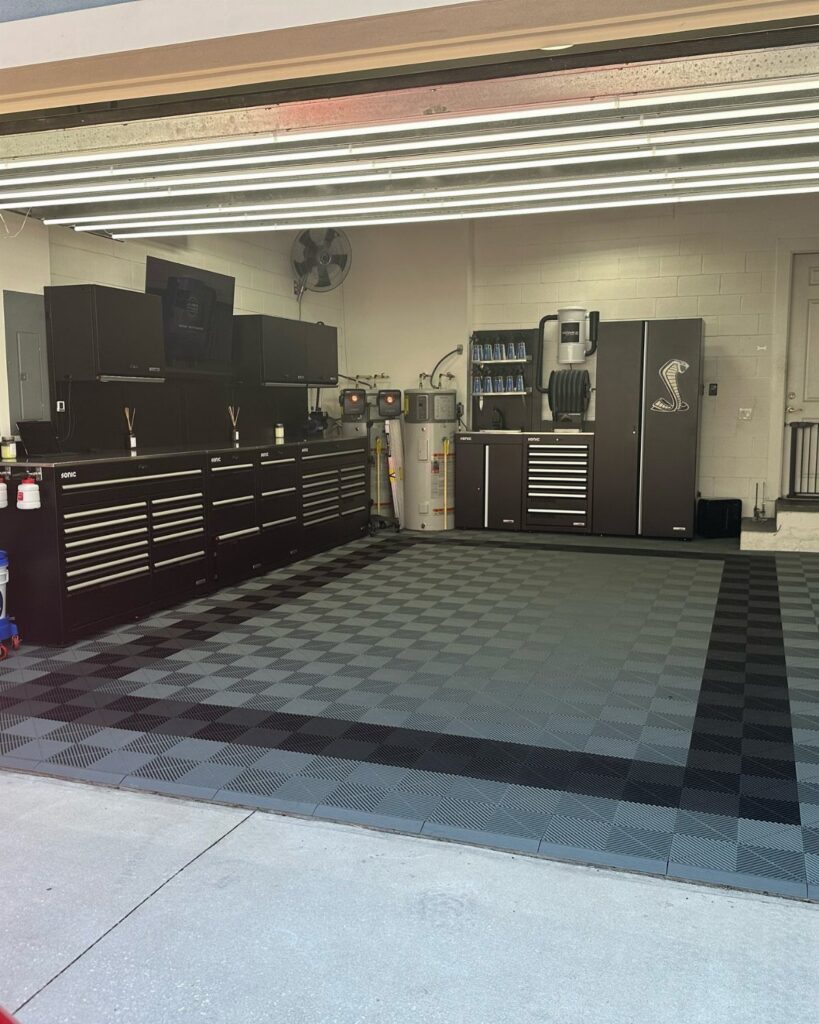 Organized garage with black tool cabinets, workbenches, and a checkered grey and black floor mat.