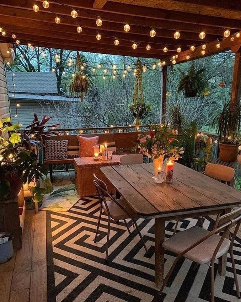 A cozy wooden deck with a dining table, string lights, and lush greenery under a wooden ceiling.