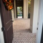 Red and tan bricks laid in a herringbone pattern on a narrow outdoor porch walkway.