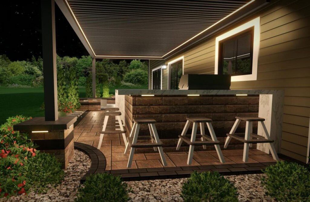 Modern outdoor kitchen with a stone bar, white stools, and a pergola on a stone patio.