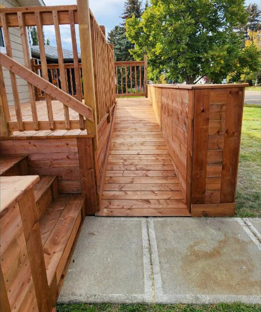 A wooden deck ramp constructed from light brown planks connecting a concrete path to a raised deck.