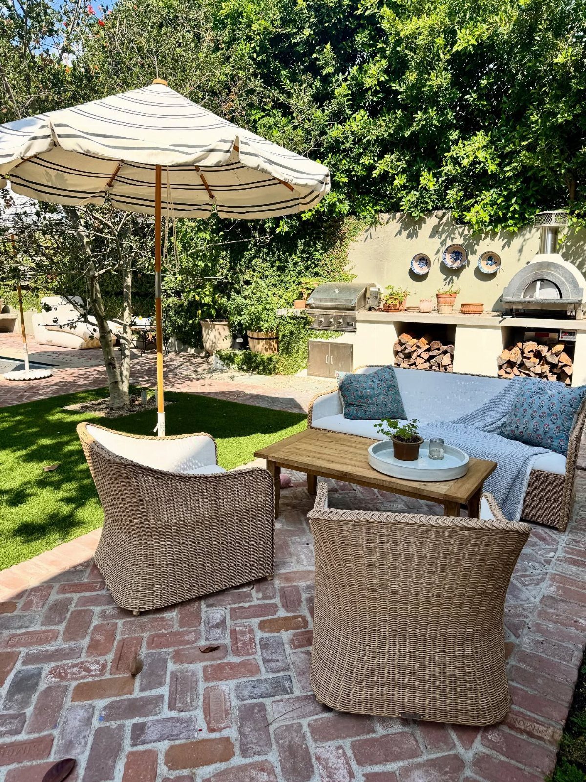 Wicker armchairs and a white sofa arranged around a wooden coffee table on a brick patio.