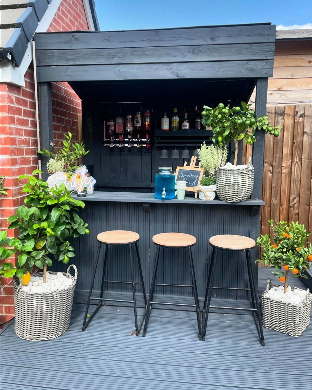 Outdoor dark grey bar station with three stools and potted citrus plants on a deck.