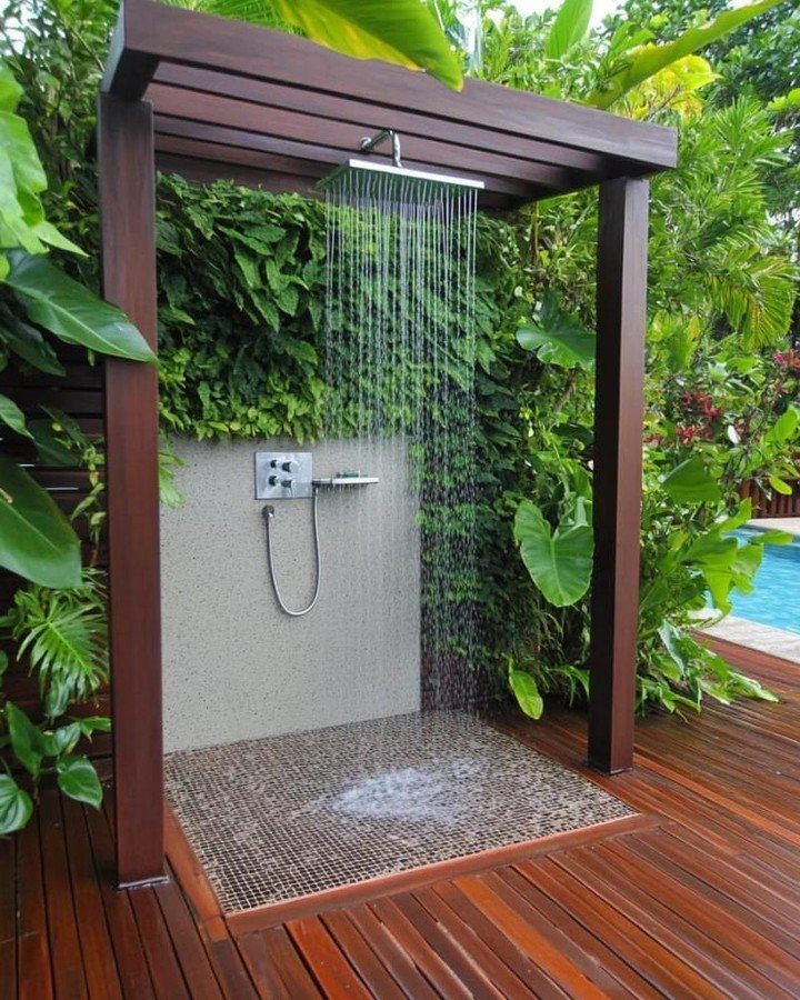 Outdoor shower with a rainfall head, wooden pergola, and lush tropical greenery on a wooden deck.