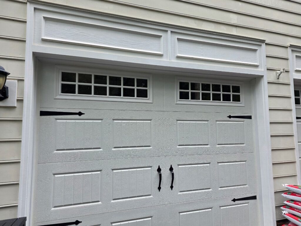 White paneled garage door with small windows and decorative black hardware on a house.