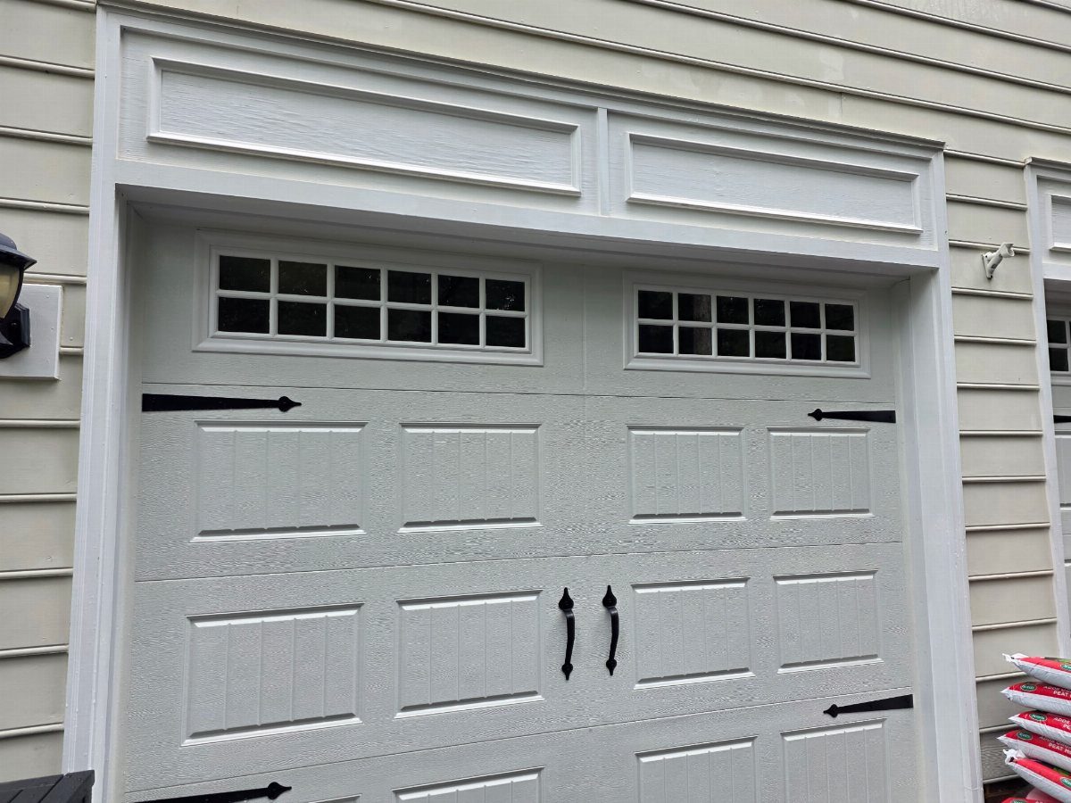 White paneled garage door with small windows and decorative black hardware on a house.